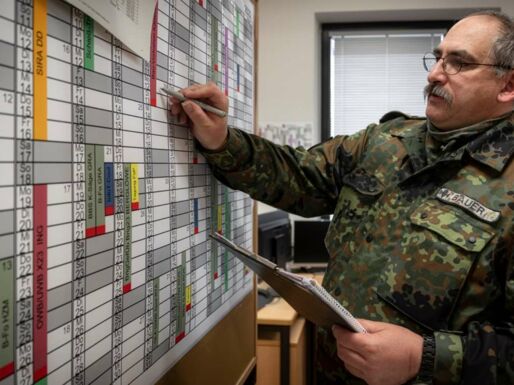 Mit einem Schreibblock in der Hand steht ein Soldat im Büro an einer Planungswand