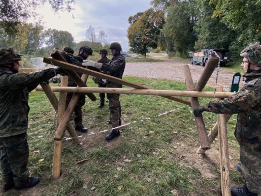 Soldaten bauen einen Spanischen Reiter aus Holzbalken und Bandstacheldraht.
